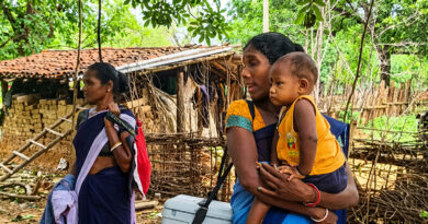 Balancing motherhood and public service, an ASHA worker carried her child in her arms while shouldering a polio vaccine box, exemplifying dedication to both her maternal responsibilities and government healthcare duties.